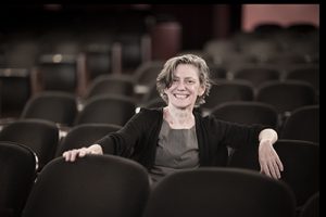 Karin Coonrod is shown sitting in a theatre.