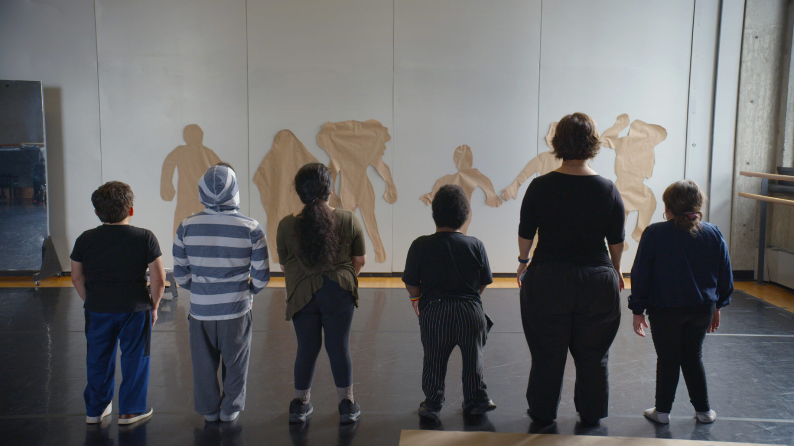 A group of six LP (little people) performers regard their paper body cut outs on the wall.
